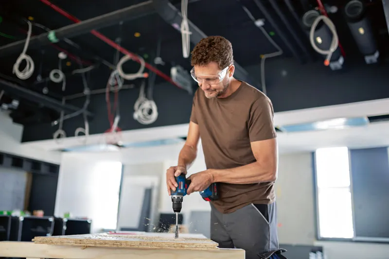 En person iført sikkerhedsudstyr borer i et panel på en byggeplads.